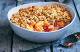 A baking dish of peach crisp with a golden almond topping